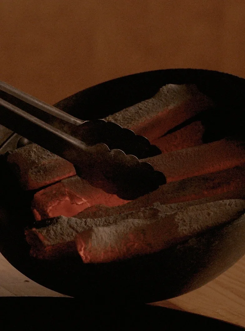 Slices of meat held with tongs over glowing charcoal