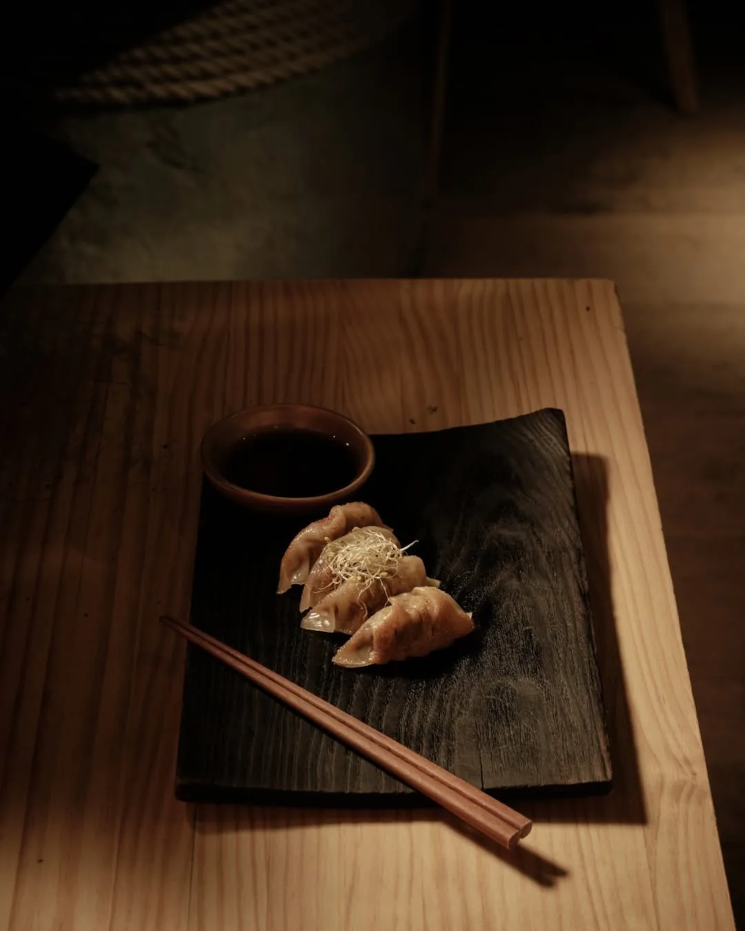 Gyoza on a dark wooden tray with a small dish of dipping sauce and chopsticks