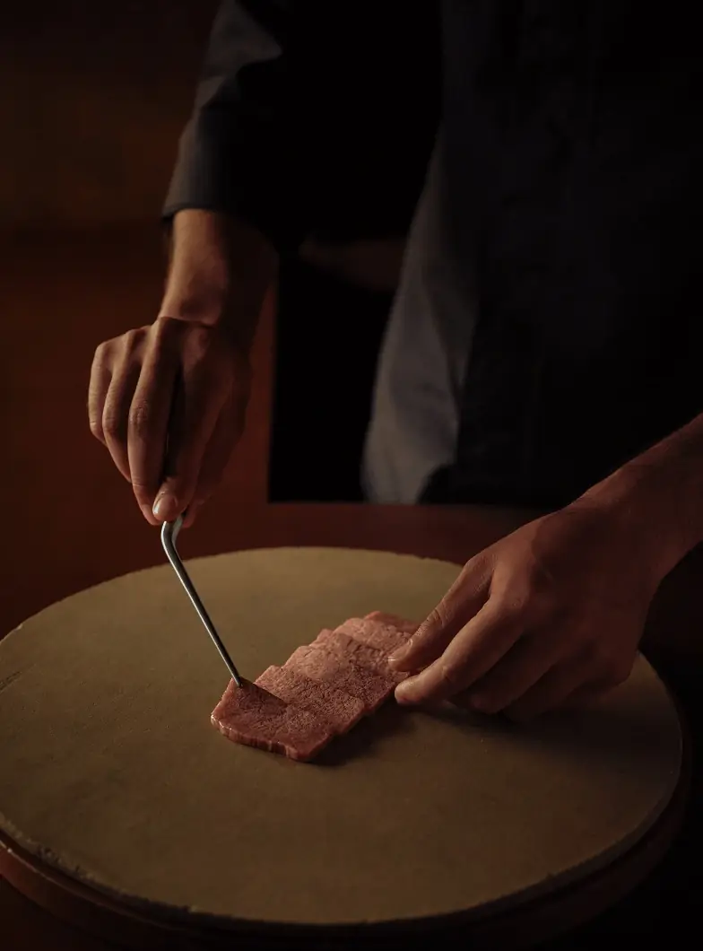 Hands arranging thin marbled wagyu beef slices on a round stone plate with a small pick