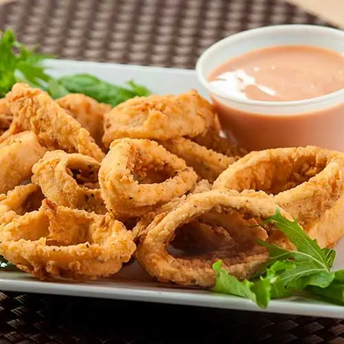 Fried calamari rings served with a lettuce garnish and a small pot of pink sauce, Piolindo