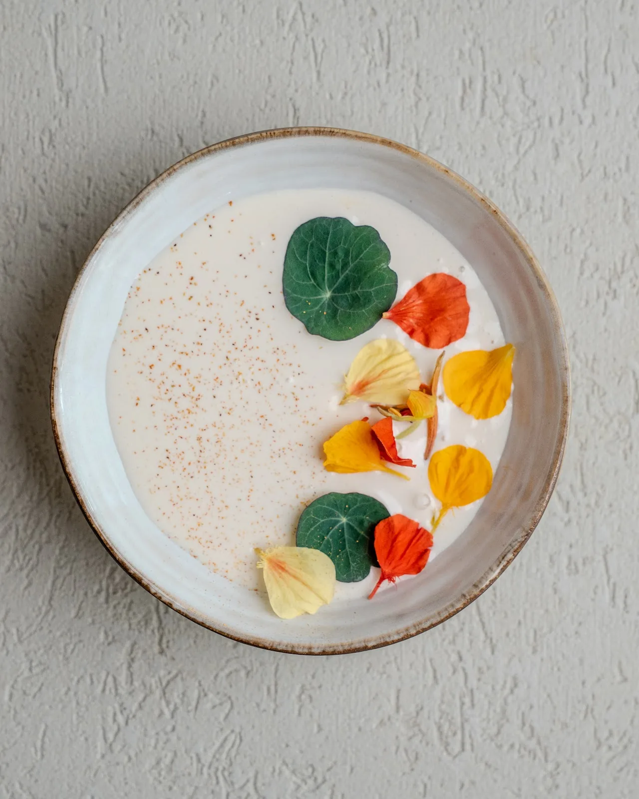 A white plate with a creamy dish garnished with colorful edible flowers