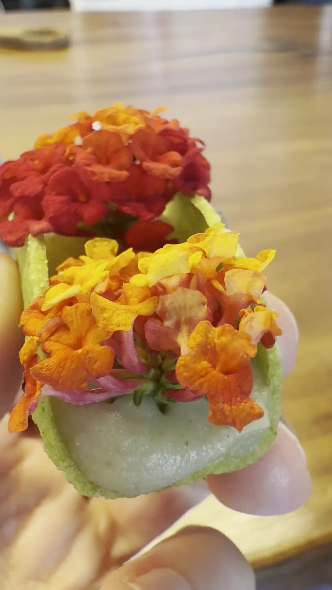 A small bite topped with an edible flower, held in a hand