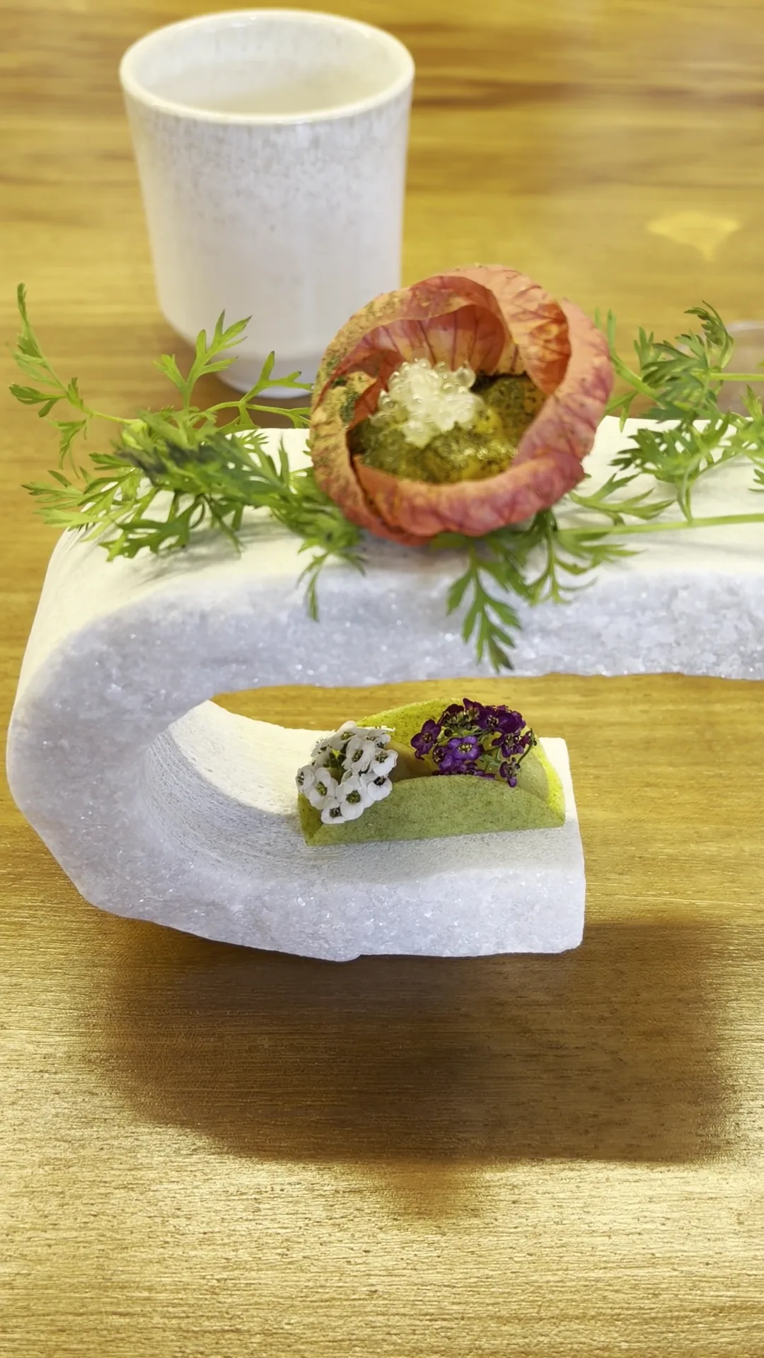 A small appetizer garnished with a flower, served on a curved white dish