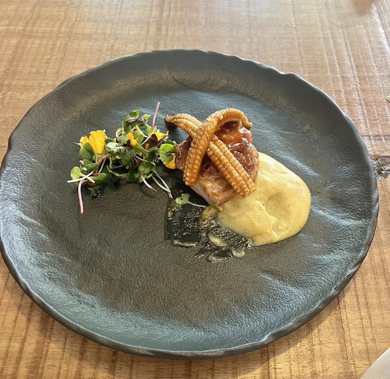 A plated dish with a seared piece of food and yellow puree