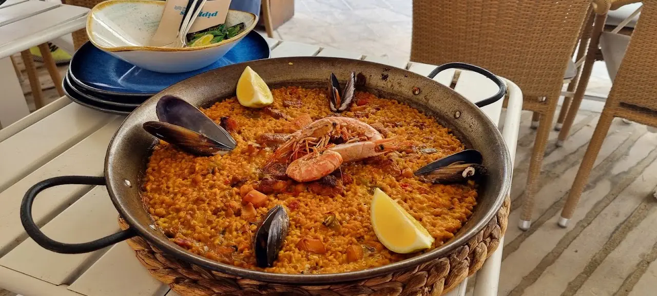 Seafood paella with mussels and prawns in a metal pan with lemon wedges.