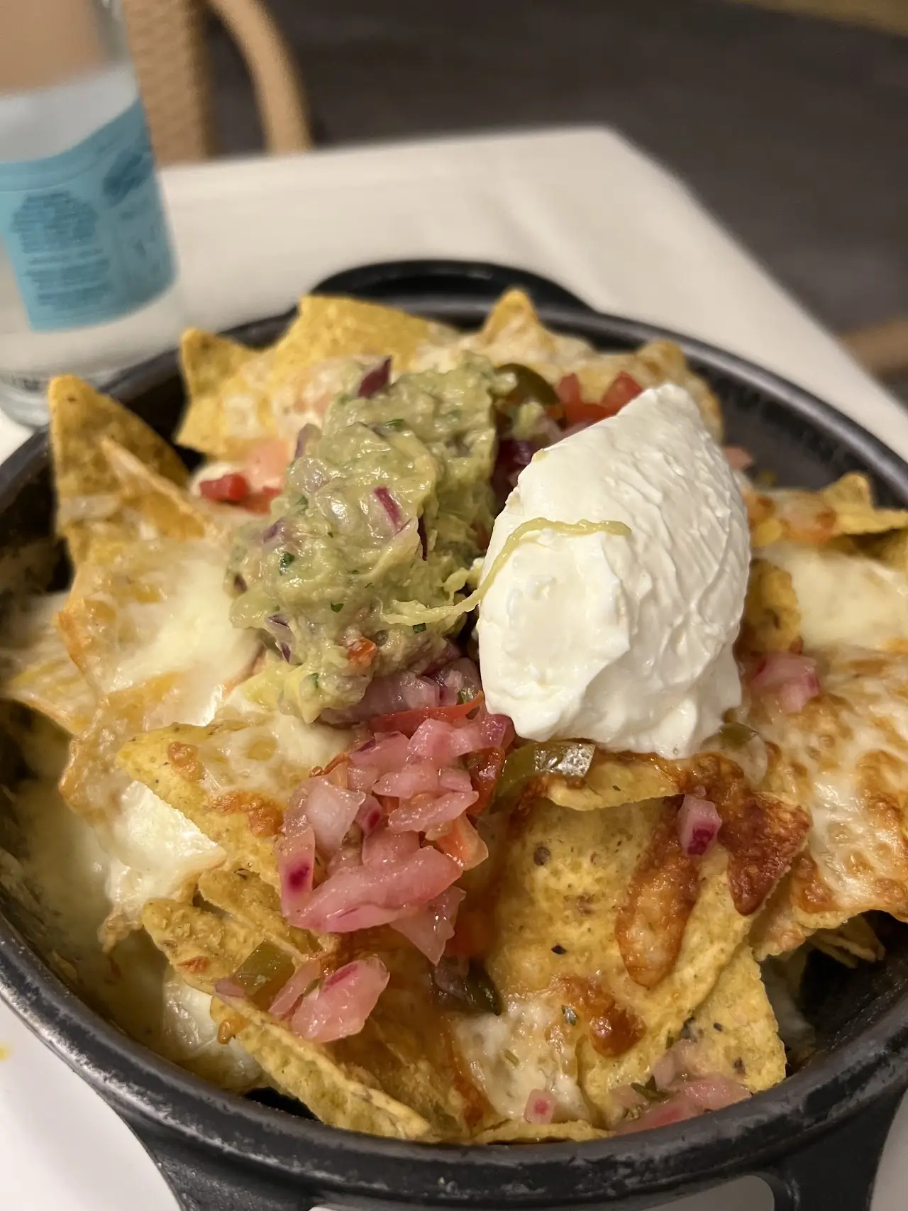 Nachos topped with melted cheese, guacamole, sour cream, and diced tomato in a skillet.