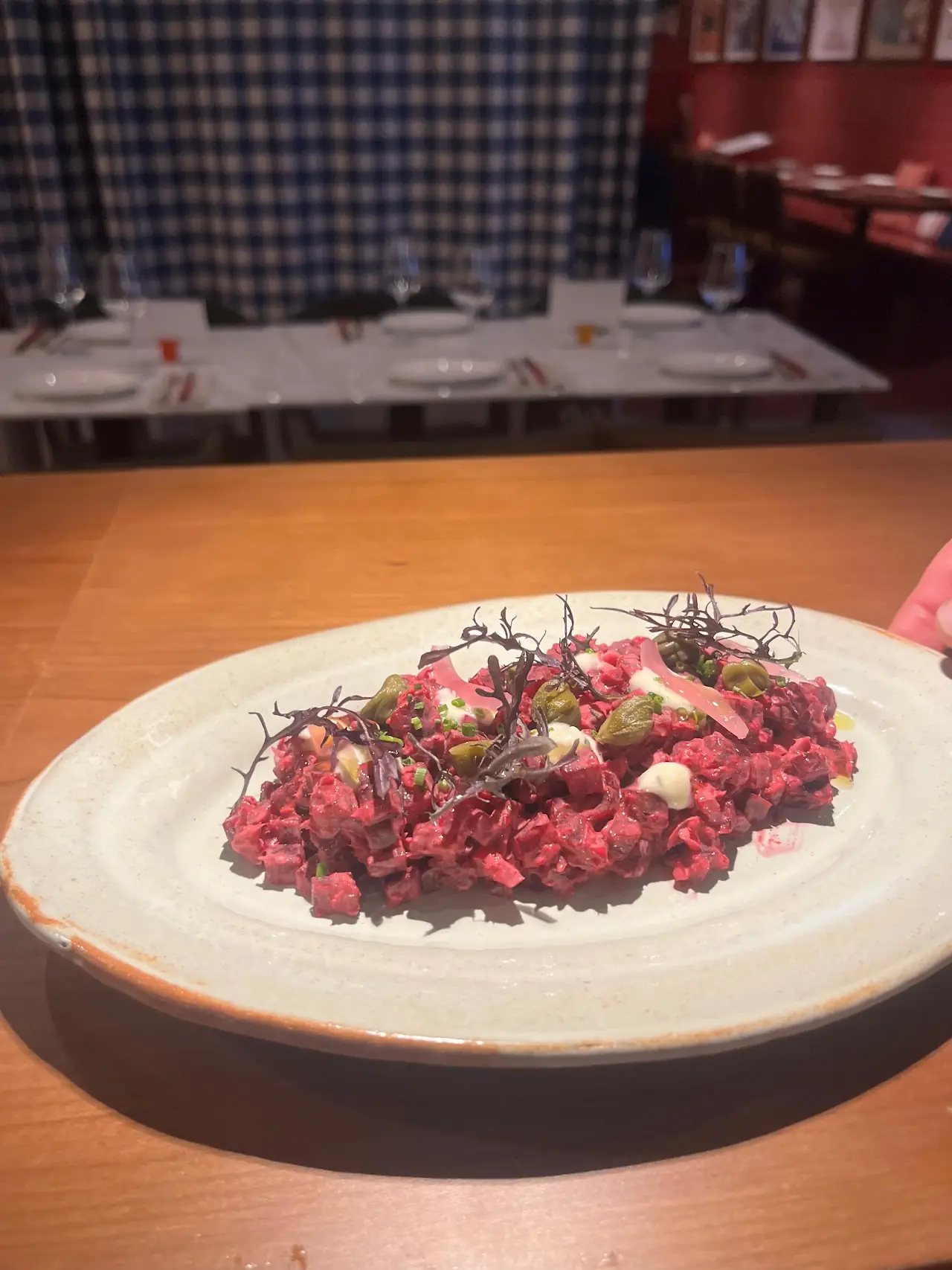 Beef steak tartare topped with microgreens and a pickled garnish on a white plate, at Piropo Bistro.