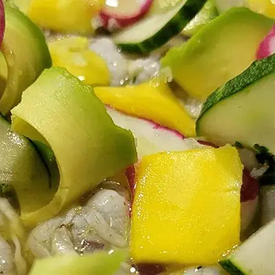 Close-up of a ceviche or salad with cubed mango, curled cucumber ribbons, radish and seafood