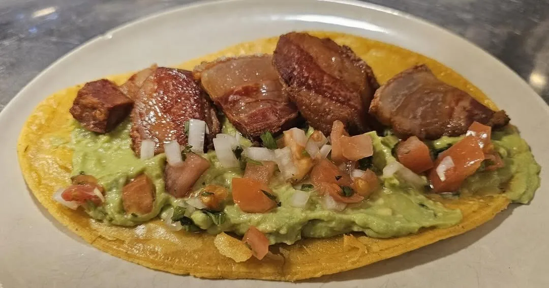 A tortilla topped with guacamole, diced tomato and pieces of grilled beef on a plate
