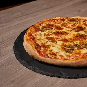 Whole margherita pizza with melted cheese and oregano on a round slate board over a wooden table
