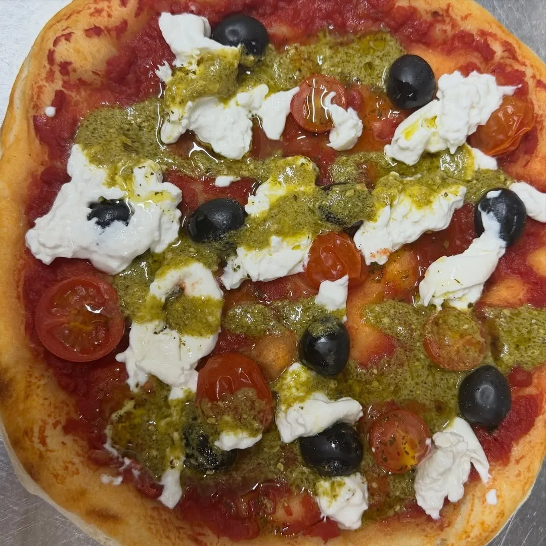 A pizza topped with green pesto, white cheese, black olives and tomatoes, seen from above