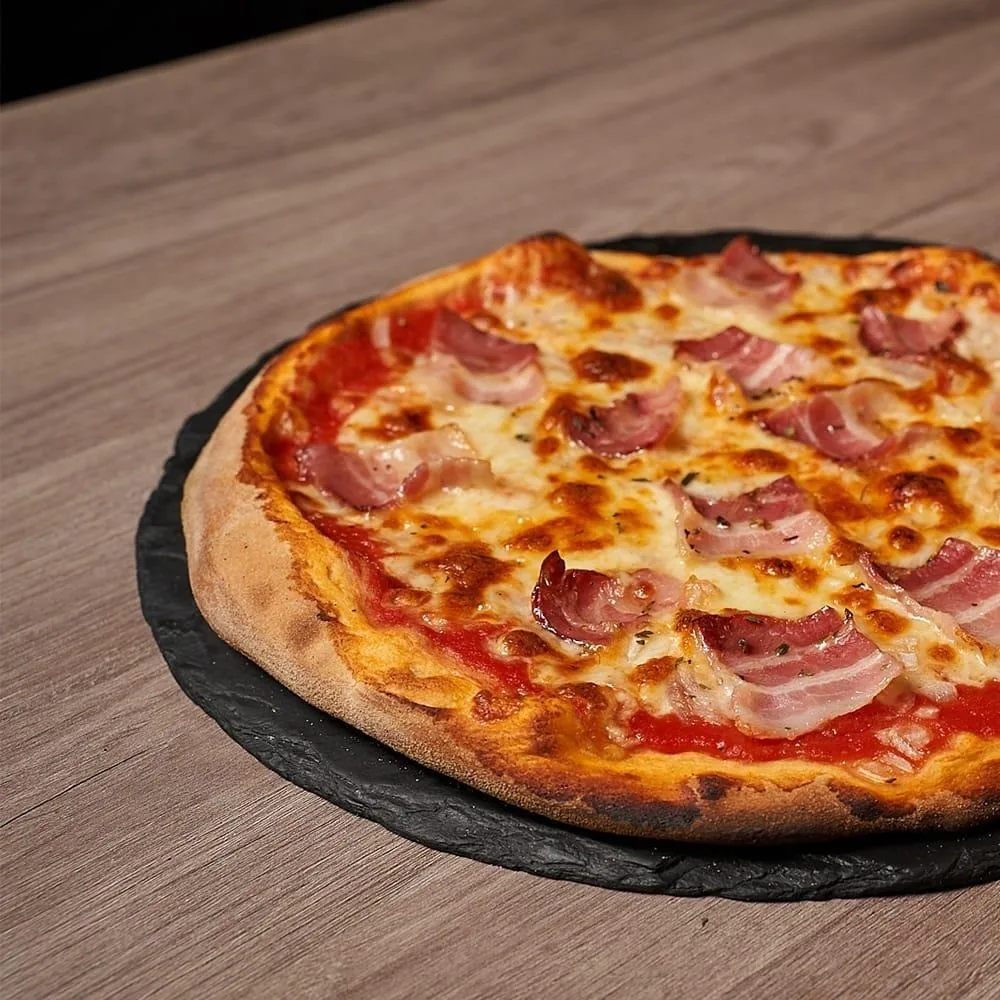 A pizza with ham and cheese on a dark slate board on a wooden table