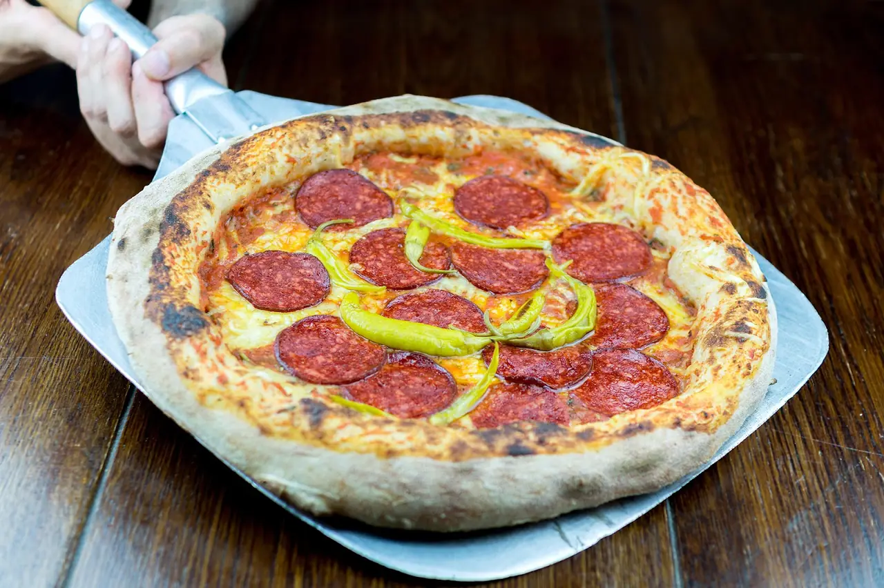 Pepperoni pizza with green guindilla peppers, held on a metal peel