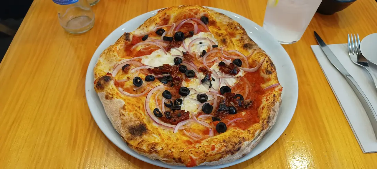 Pizza topped with black olives, red onion and sun-dried tomatoes on a table