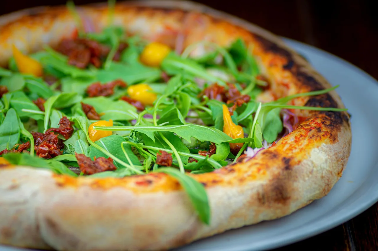 A pizza topped with rocket, sun-dried tomatoes and yellow peppers on a grey plate
