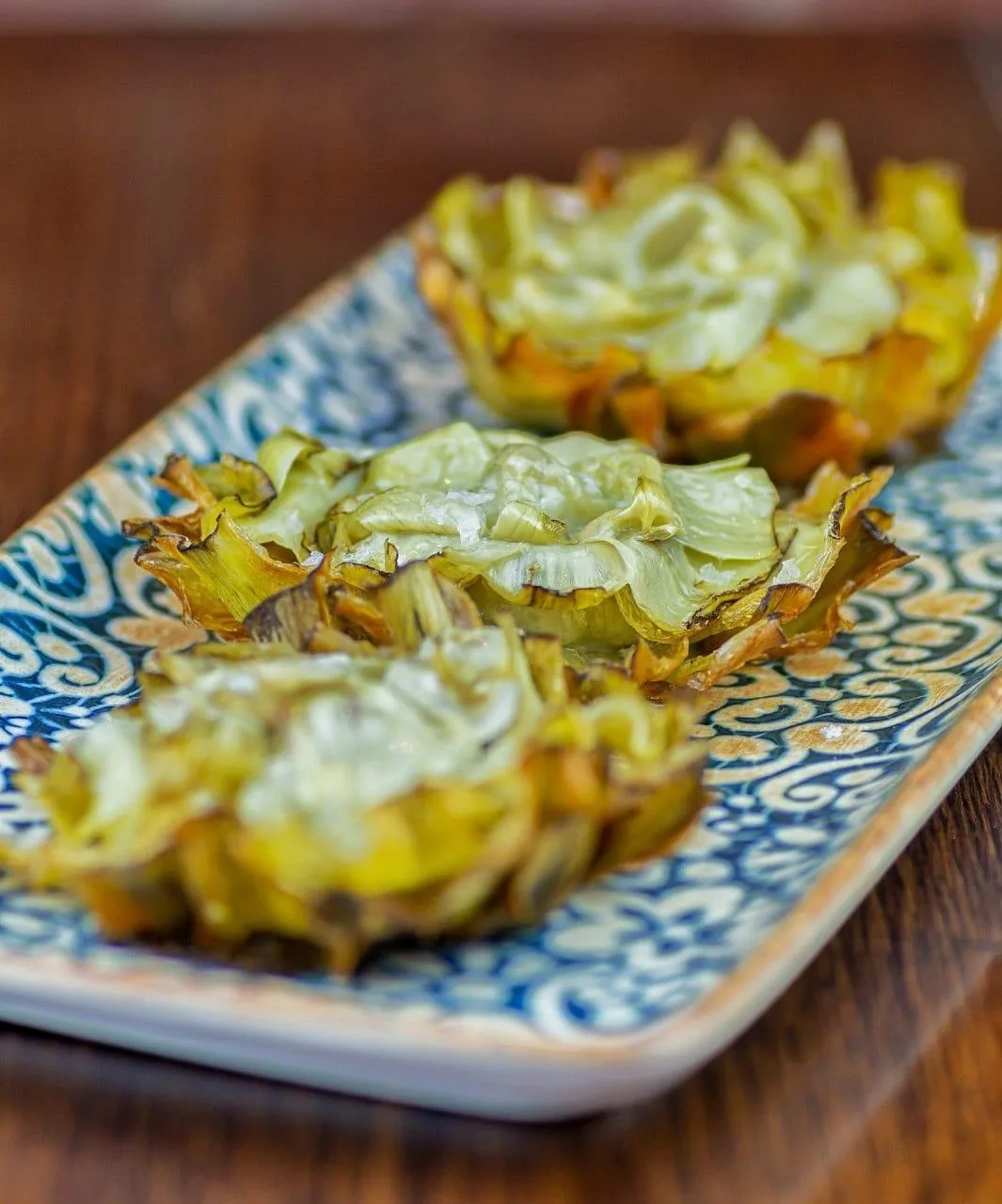 Three golden fried artichokes on a blue and white patterned plate