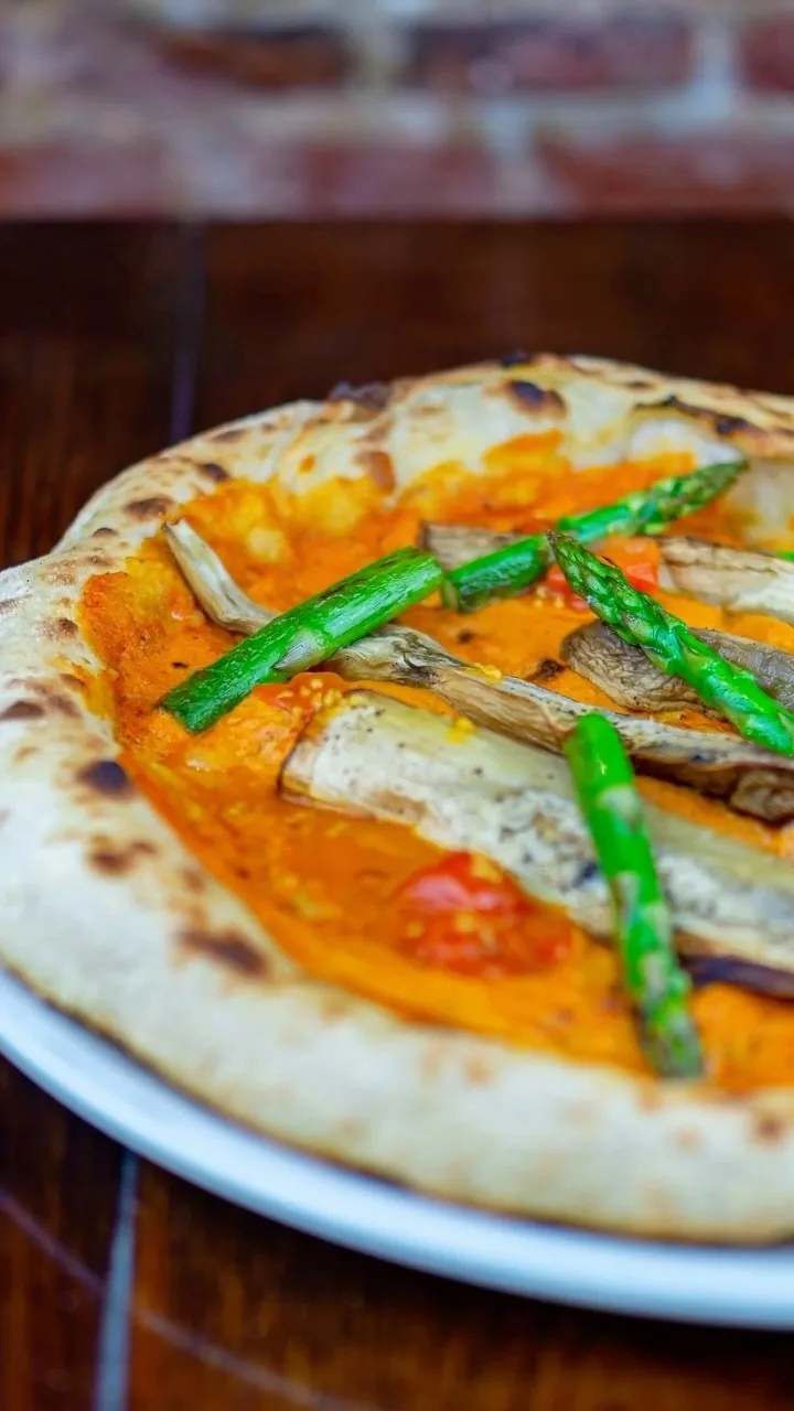 A pizza with an orange sauce, grilled asparagus spears and slices of grilled mushroom