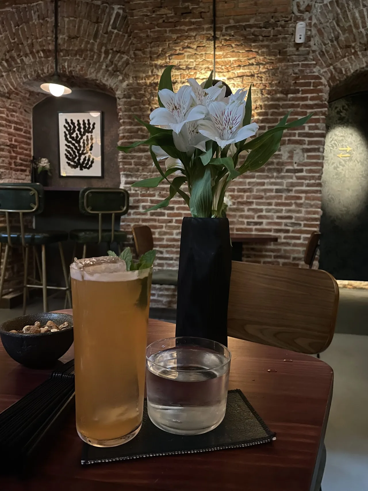 Two cocktails on a table beside a small vase of flowers