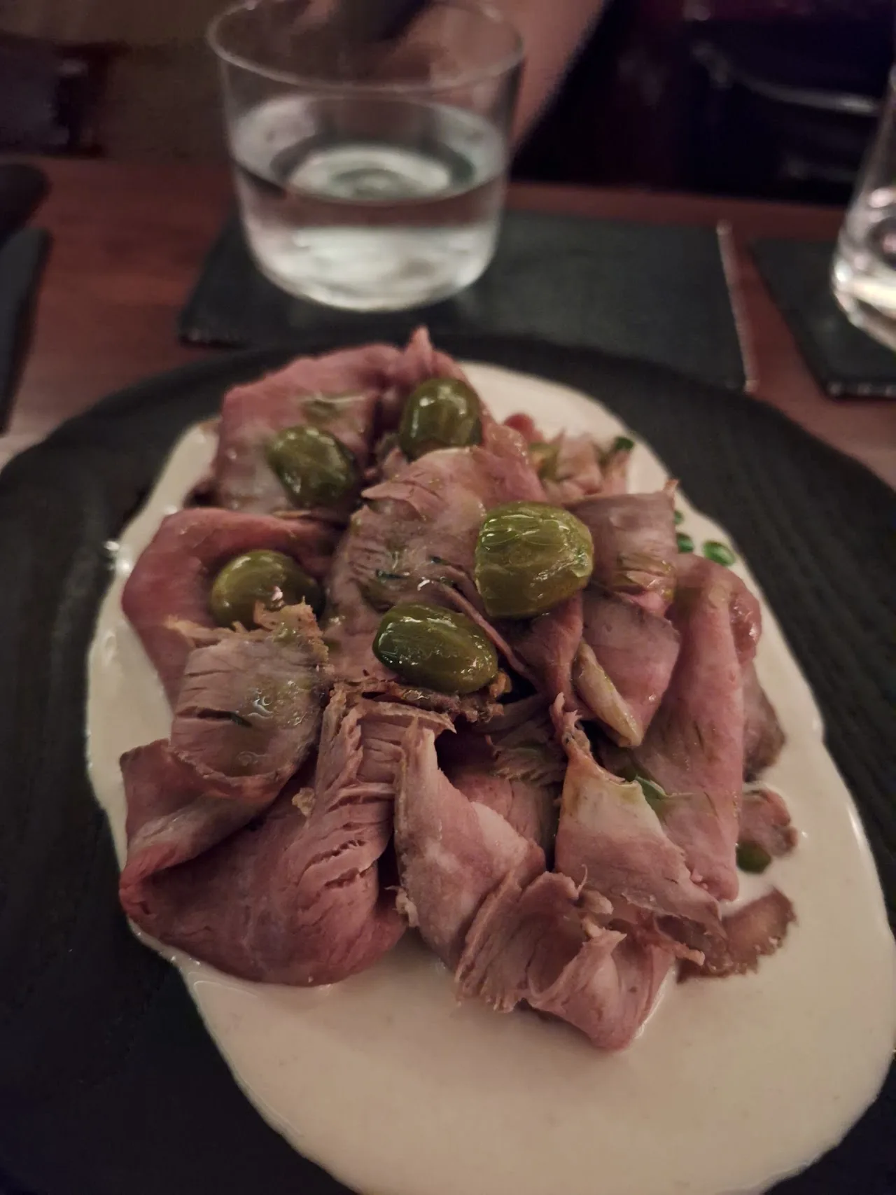 A plate of thinly sliced cured meat topped with olives