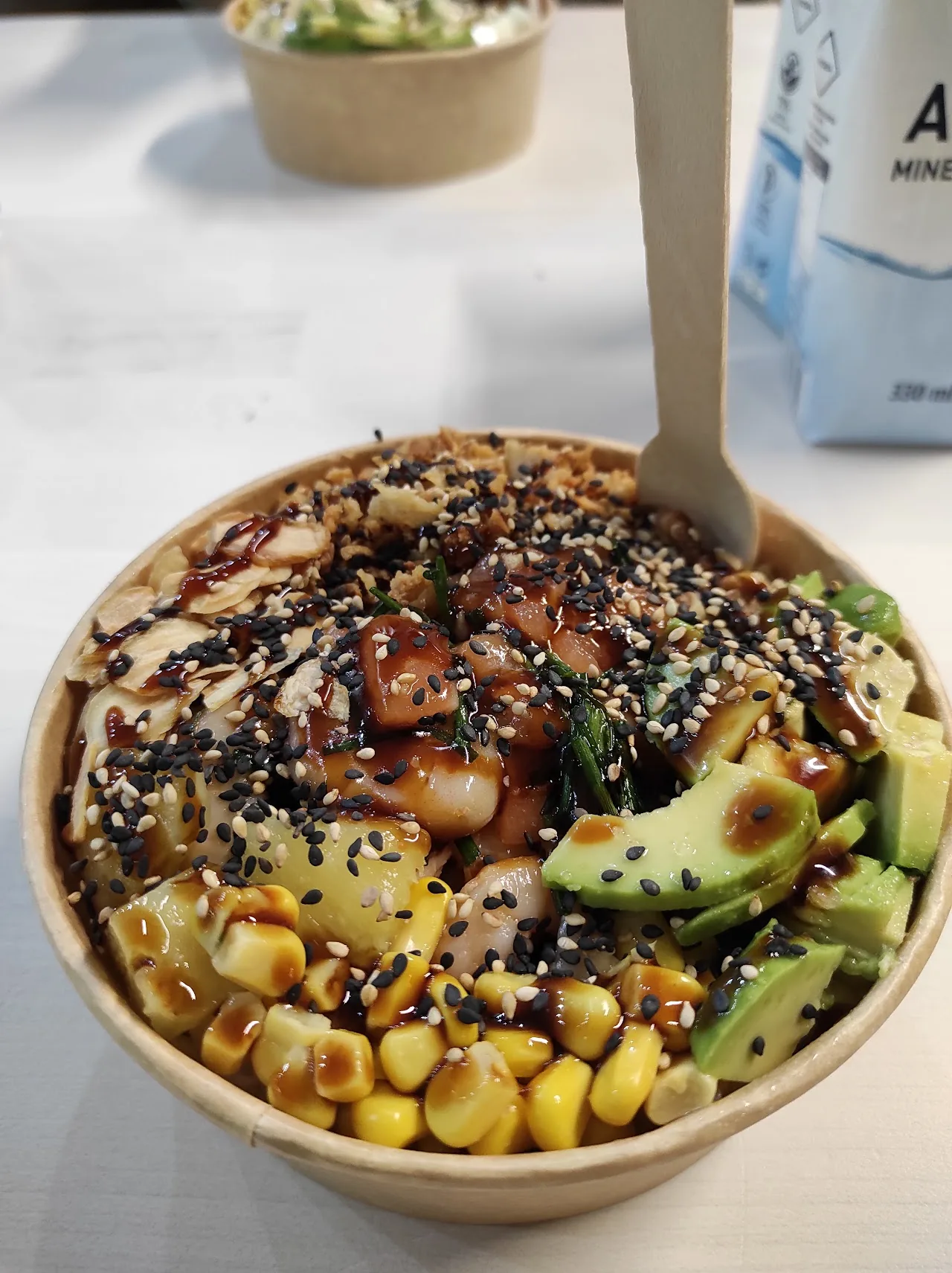 A poke bowl with salmon, avocado, corn, and sesame seeds