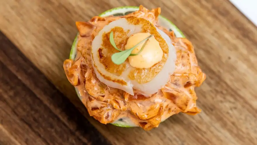 Seared scallop with sauce dollop over shredded seafood salad on a lime shell