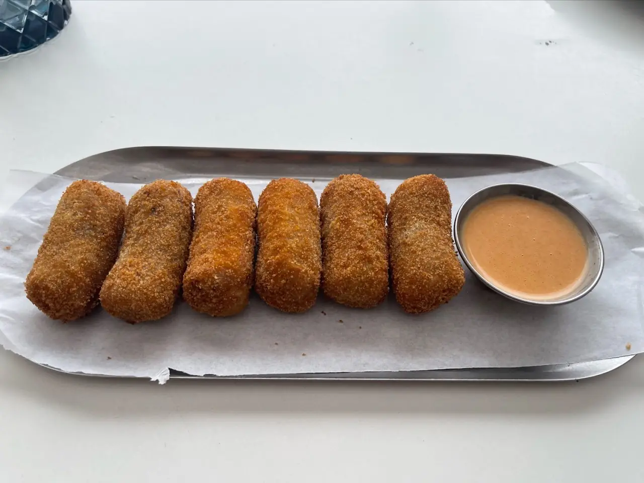 Six breaded fried croquettes on a tray with a dipping sauce.