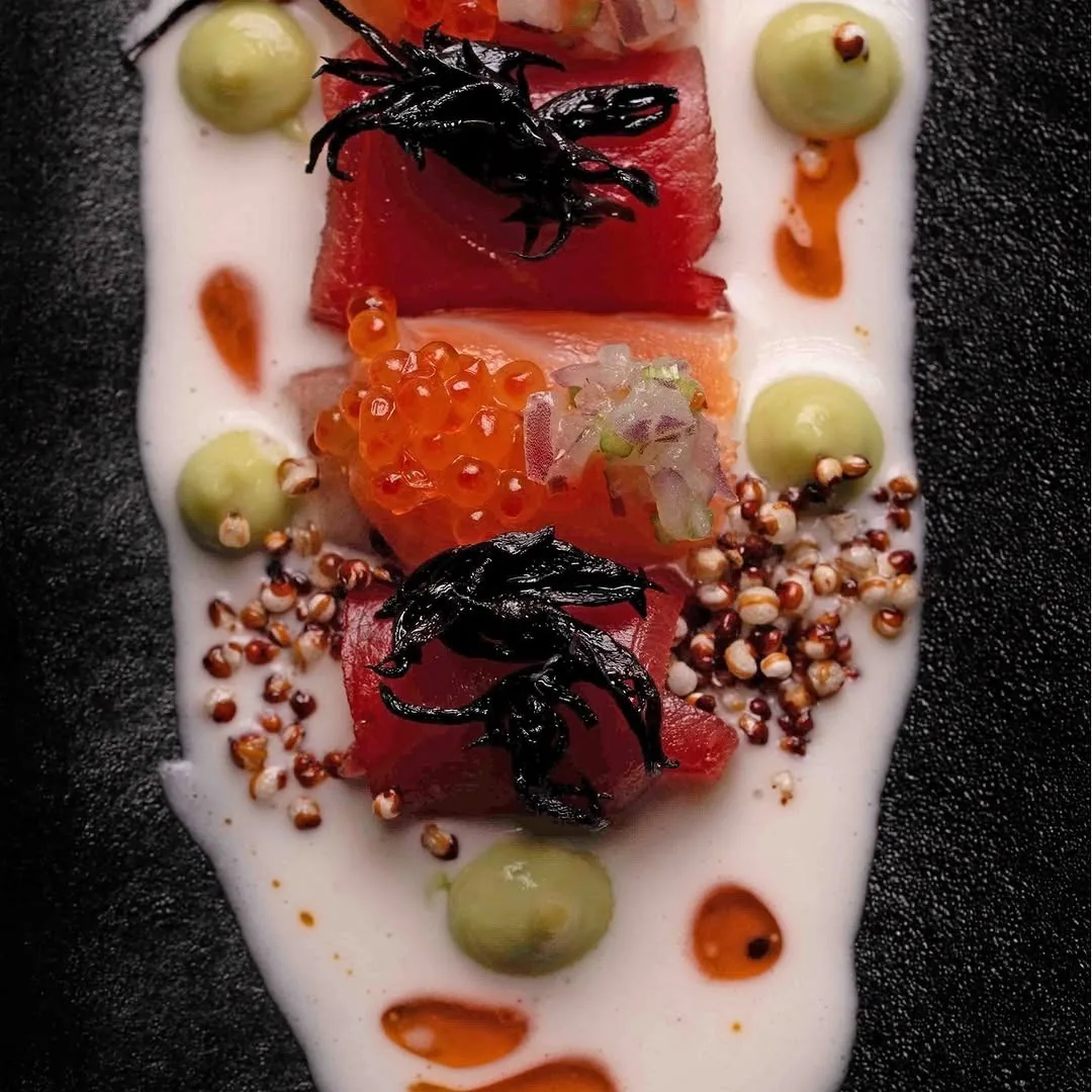 Slices of raw tuna with orange roe, green dots and grains on a white sauce