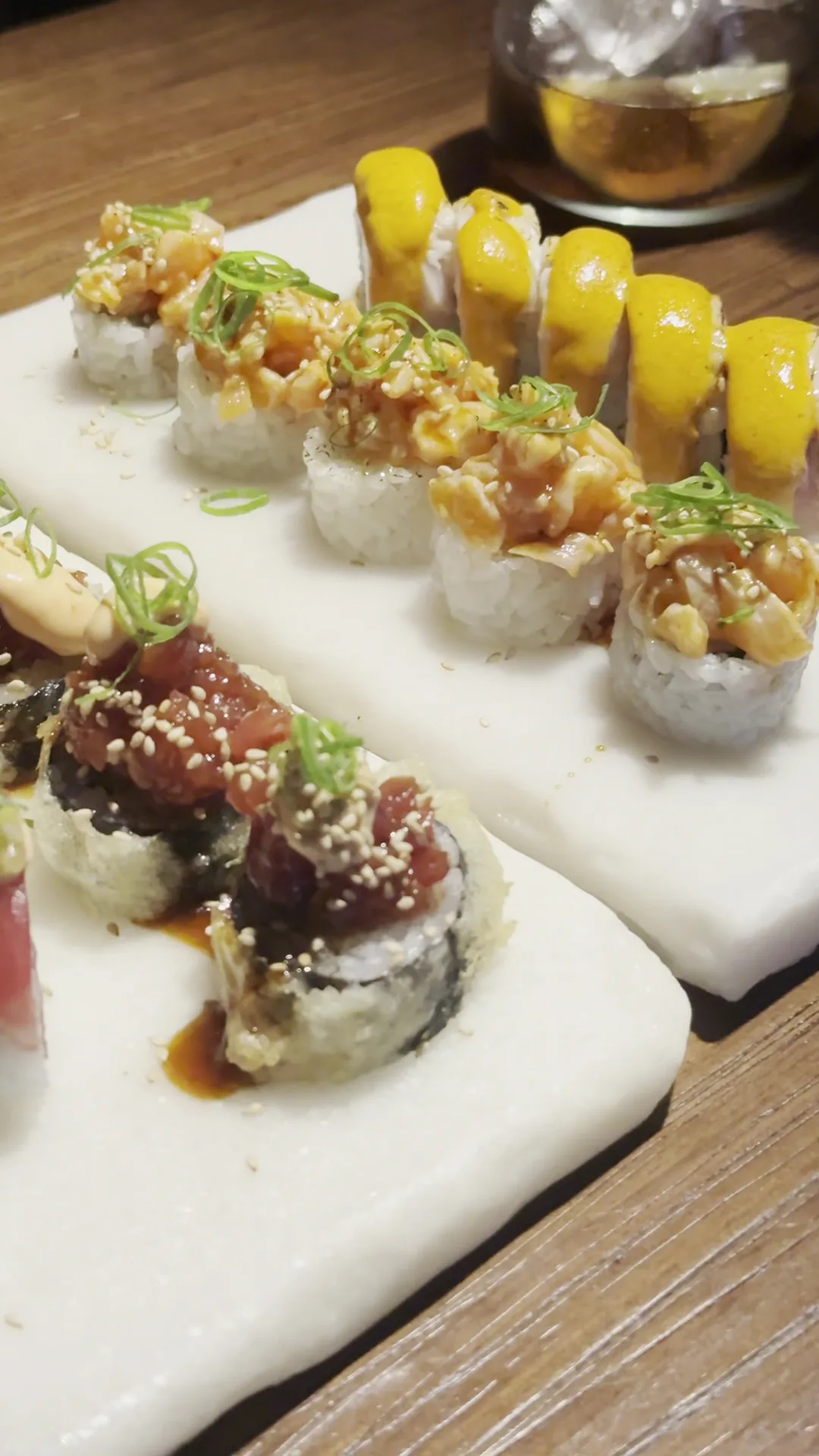 Sushi rolls topped with tuna and pineapple chunks on a wooden board