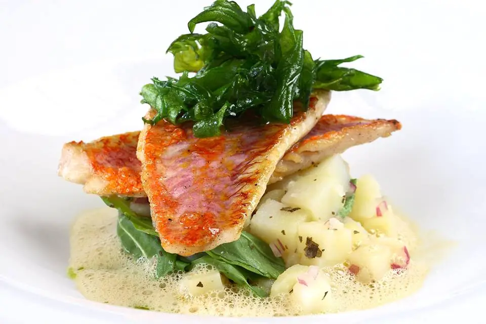 Pan-seared fish fillet over potatoes with sautéed greens and a light sauce.