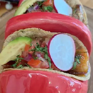 Close-up of tacos with avocado, radish and pico de gallo in a chile-shaped holder
