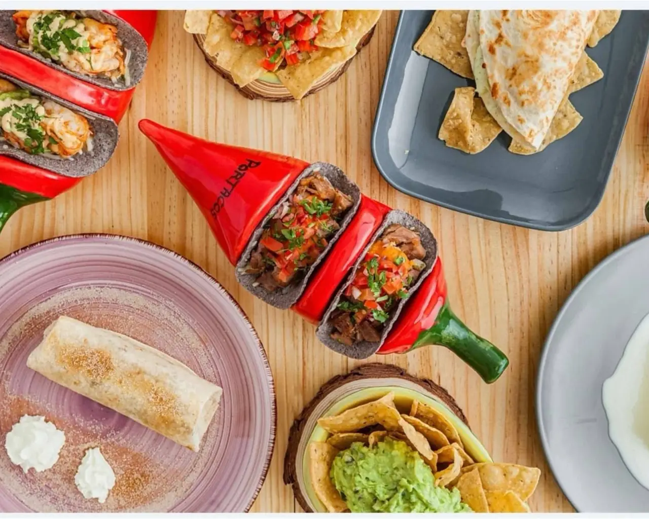 Tacos, guacamole with totopos, a quesadilla and a burrito spread on a wooden table