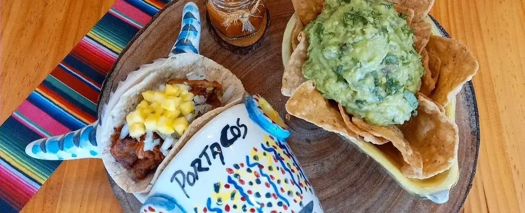 Al pastor taco with pineapple next to guacamole and tortilla chips