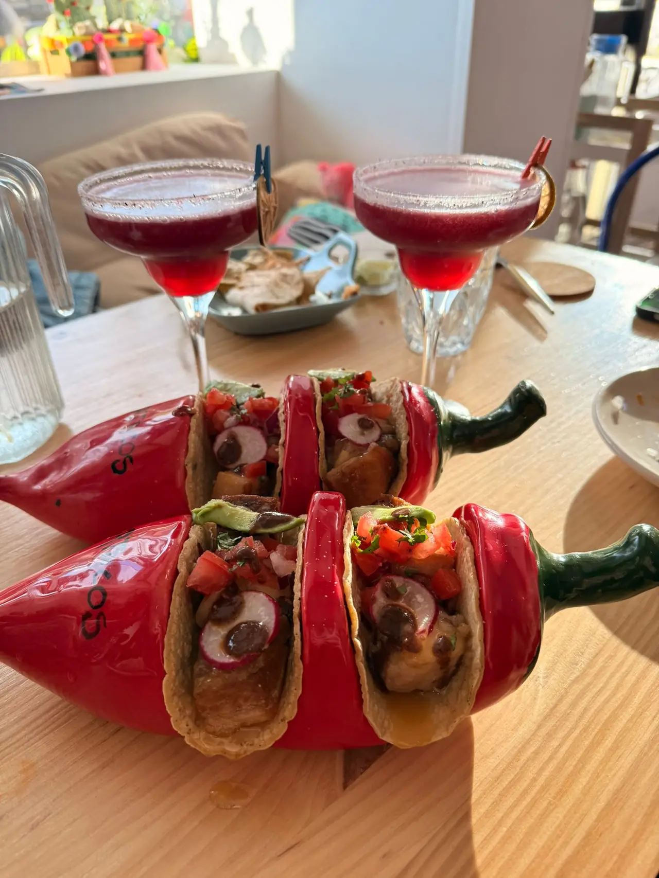 Tacos in red chilli-shaped holders with two frozen margaritas behind