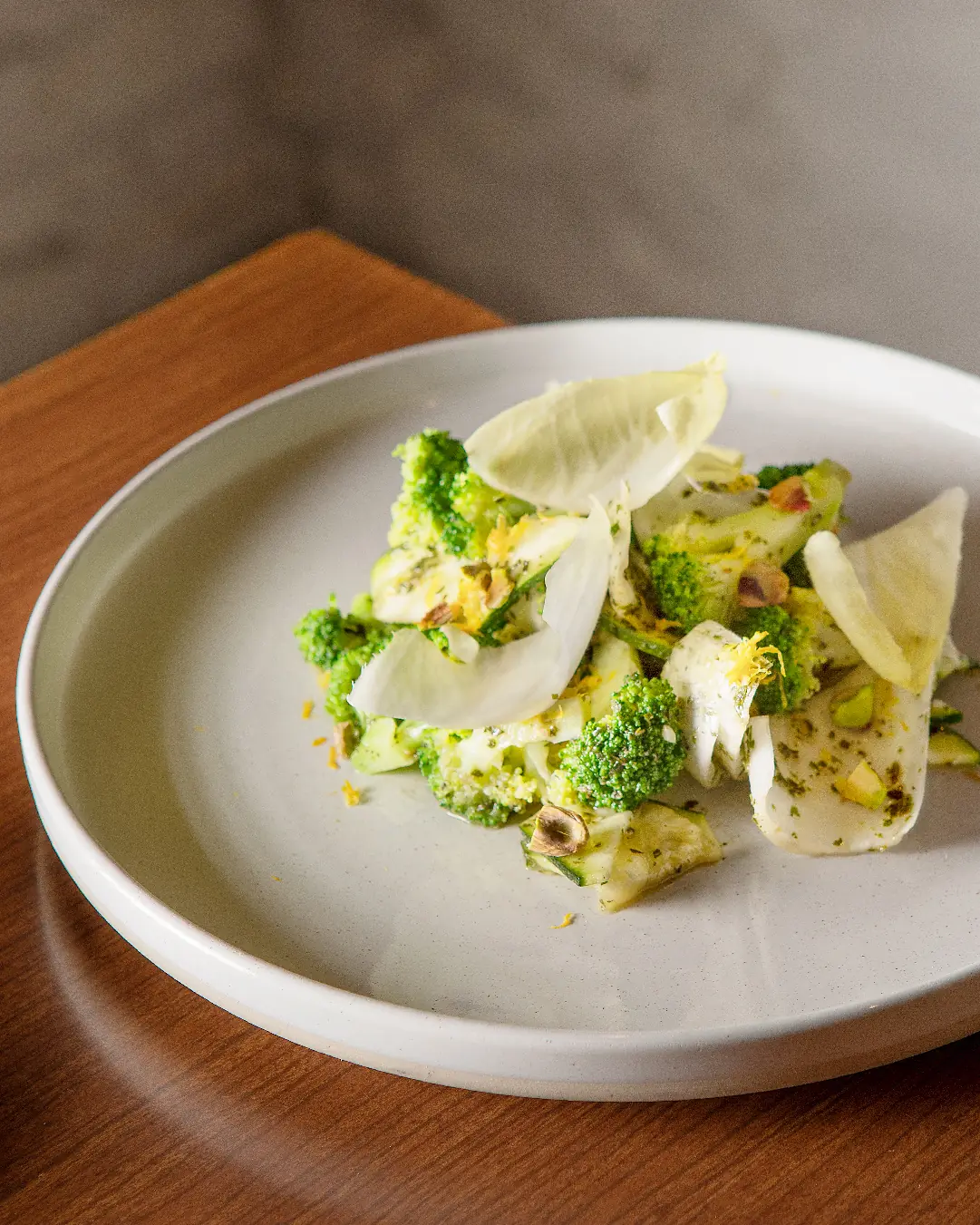 Shaved broccoli and endive salad with pistachios, hazelnuts, lemon zest and a crisp chip, on a matte white plate at PÖTSTOT