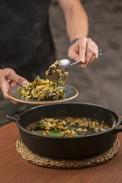 A steaming spoonful of green herb rice with beans being lifted from a cast-iron pot onto a plate at PÖTSTOT