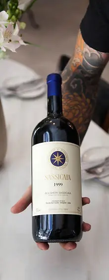 A hand presenting a magnum bottle of Sassicaia 1999 Bolgheri over a set table