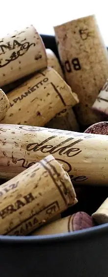 Close-up of used wine corks printed with winery names piled in a dark bucket