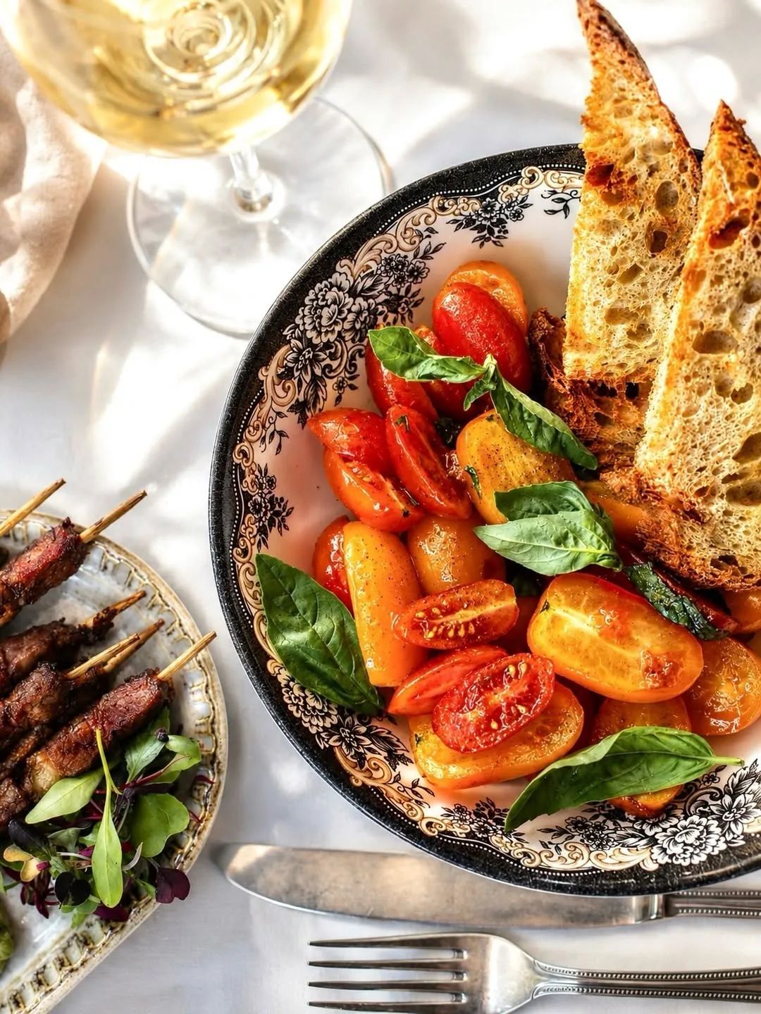 A plate of tomato salad with grilled skewers and toasted bread on a table