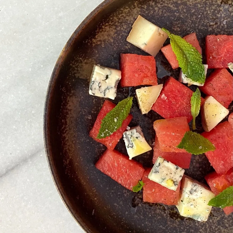 Watermelon cubes with mint and blue cheese on a dark plate