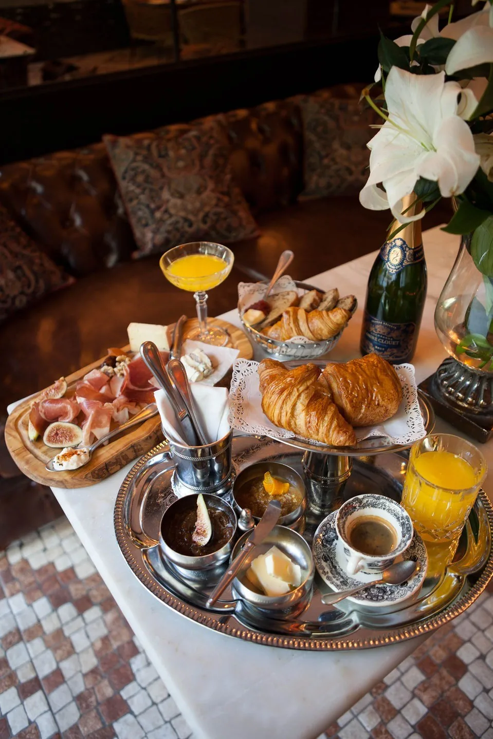 A tray of pastries, coffee cups and glasses on a tiled table