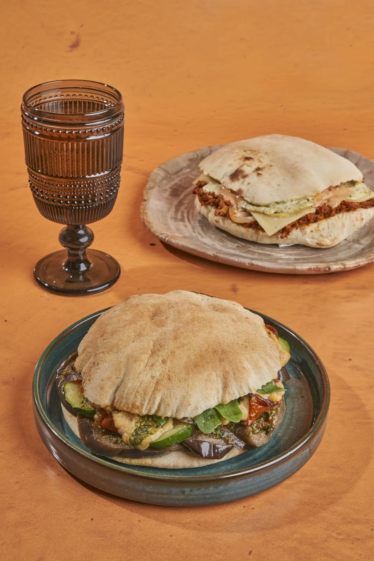 A stuffed flatbread sandwich on a plate beside a glass of wine