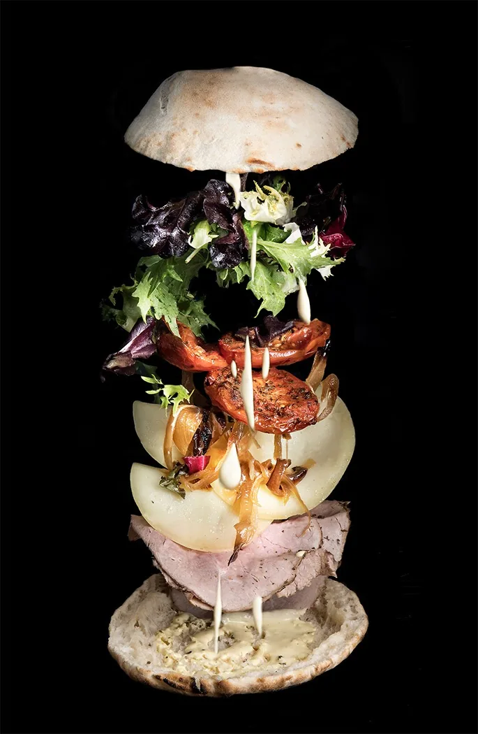 A sandwich shown as stacked ingredient layers against a black background