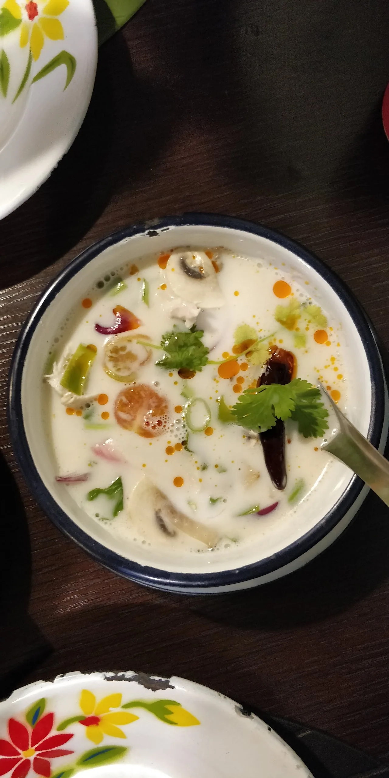 A bowl of creamy tom kha soup garnished with herbs and chili