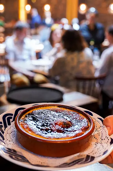 Crema catalana in a shallow clay dish with a caramelized sugar top, served on a decorative blue-and-white plate at Pulperia Can Lampazas