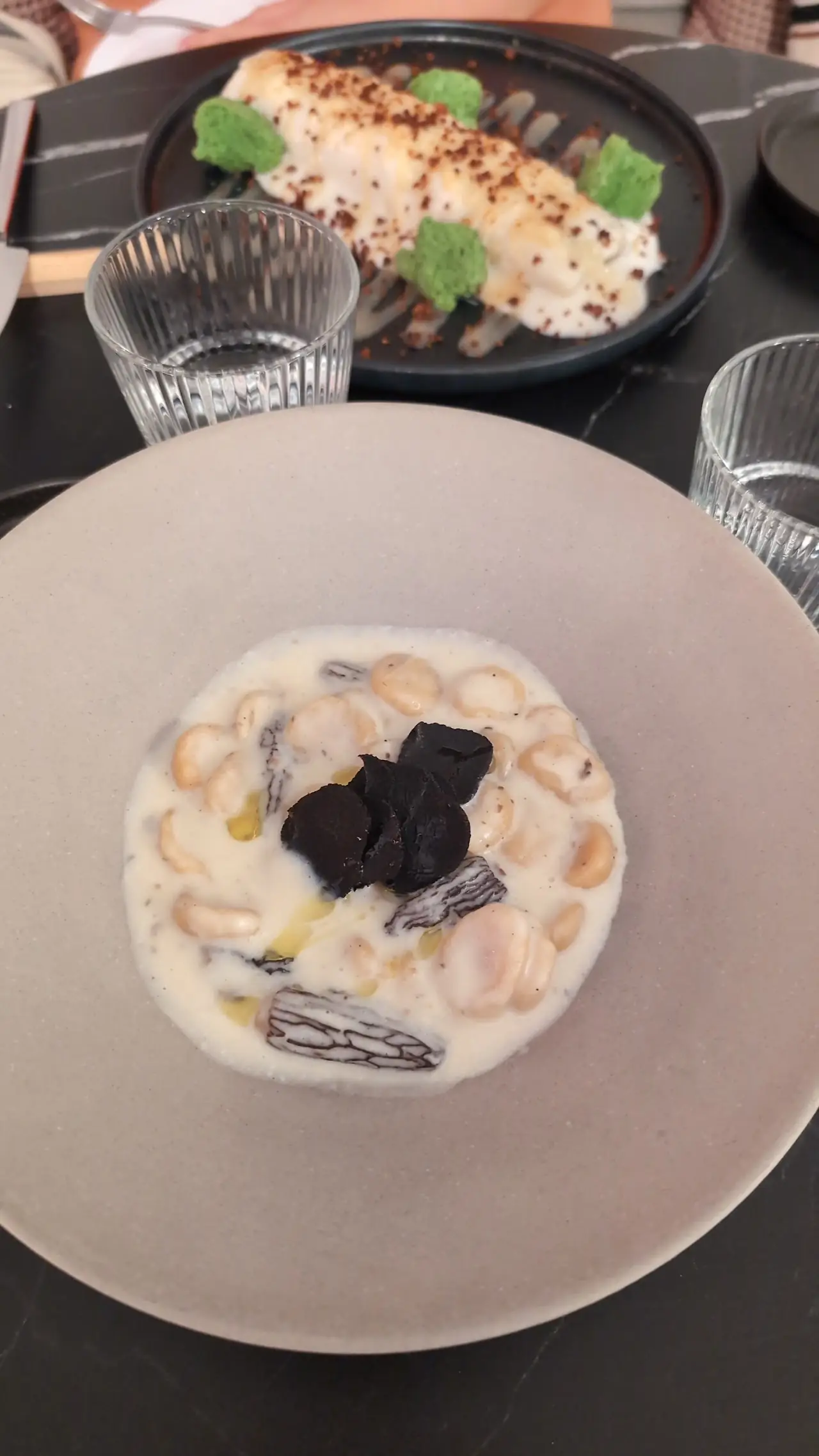 Creamy white bean stew with black shavings on top, served in a wide bowl.