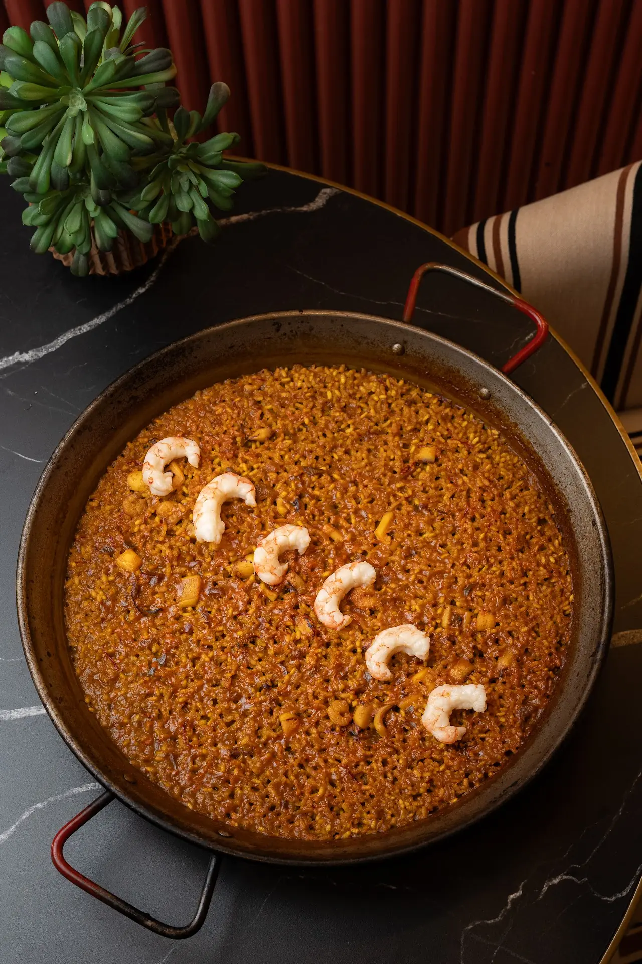 Rice dish in a paella pan topped with a row of shrimp.