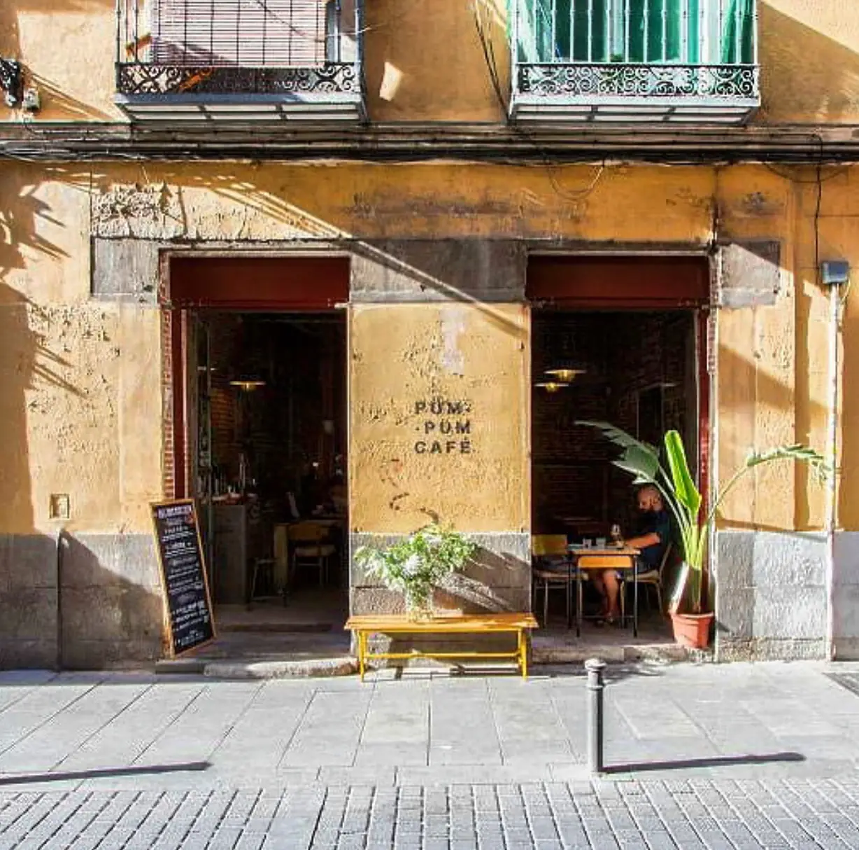 The cafe's yellow street-facing facade with open doorways, a bench, and outdoor seating