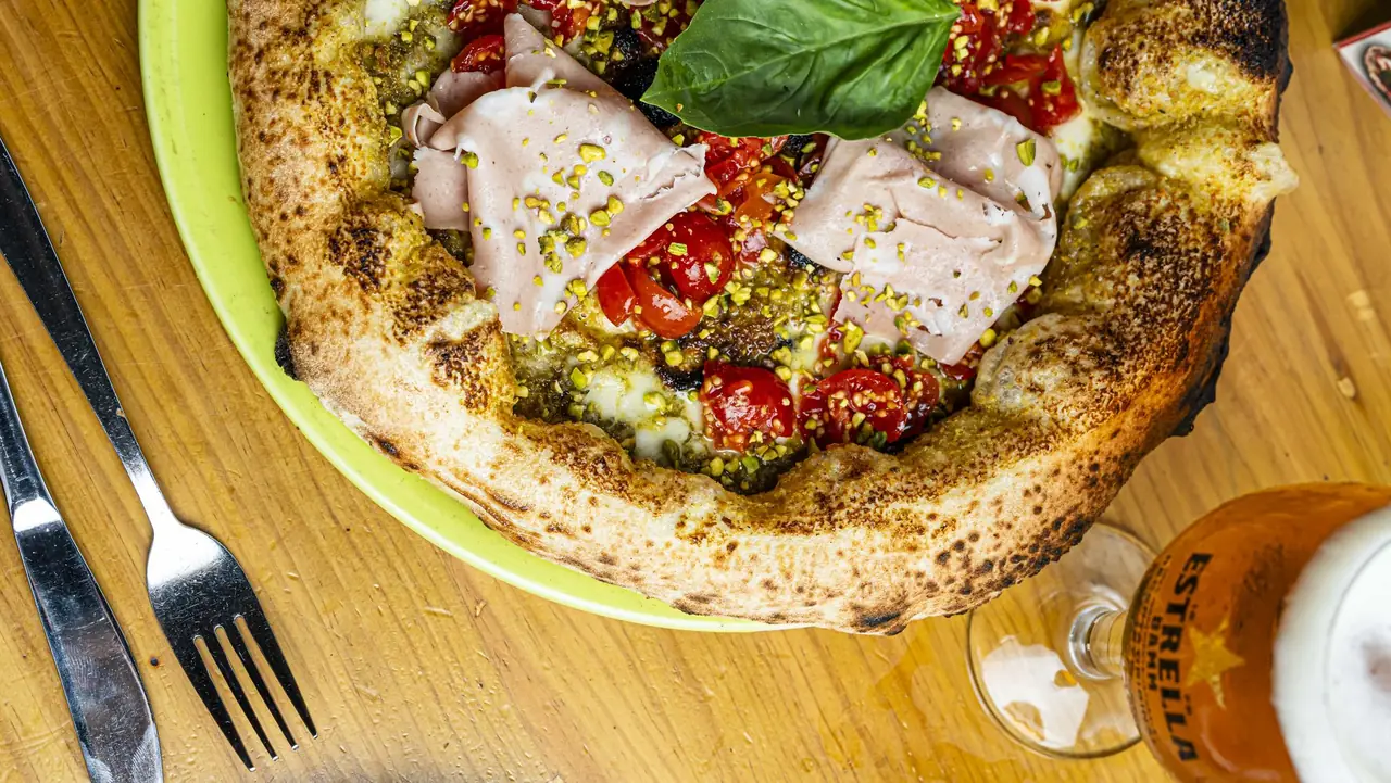 Neapolitan pizza topped with folded mortadella, cherry tomatoes, pistachio crumble, and basil, on a lime-green plate at Pummarola Pizzeria Napoletana