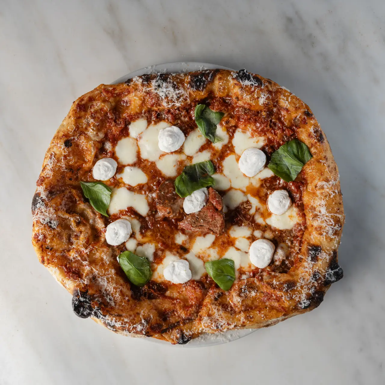 Wood-fired pizza topped with tomato sauce, melted mozzarella, dollops of burrata, basil leaves, and shaved cheese at Punta