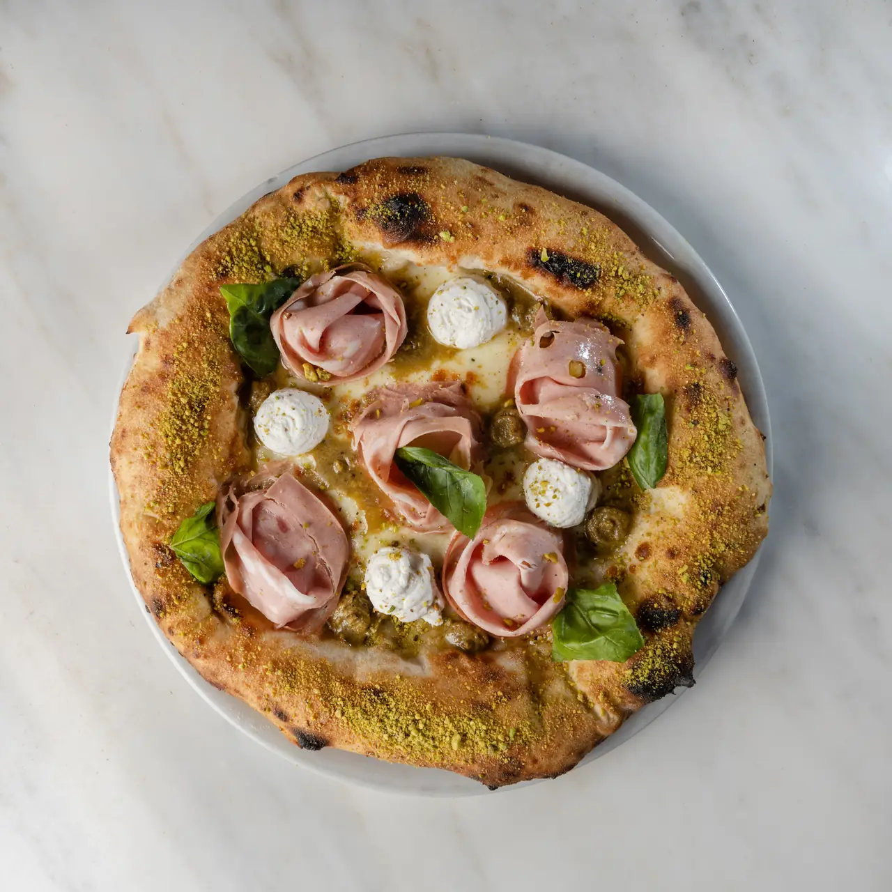 Wood-fired pizza topped with rolled cured ham, burrata dollops, olives, and basil leaves at Punta